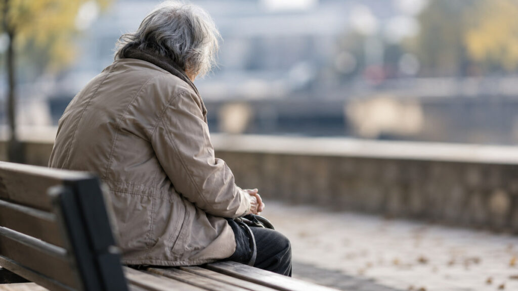 Alcalá aprueba cinco convenios sociales por 55.200 euros para atender a personas vulnerables y familias con dificultades 1 Persona mayor sentada sola de espaldas en un banco, con el entorno desenfocado.