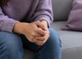 Primer plano de las manos entrelazadas de una mujer sentada, sin mostrar su rostro.
