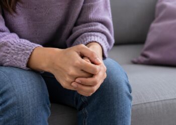 Primer plano de las manos entrelazadas de una mujer sentada, sin mostrar su rostro.