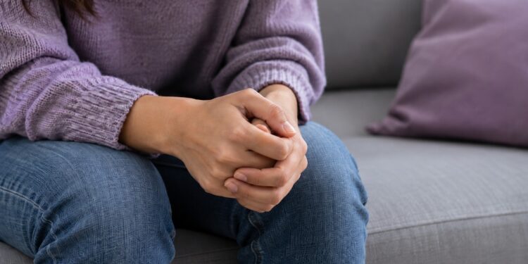Primer plano de las manos entrelazadas de una mujer sentada, sin mostrar su rostro.